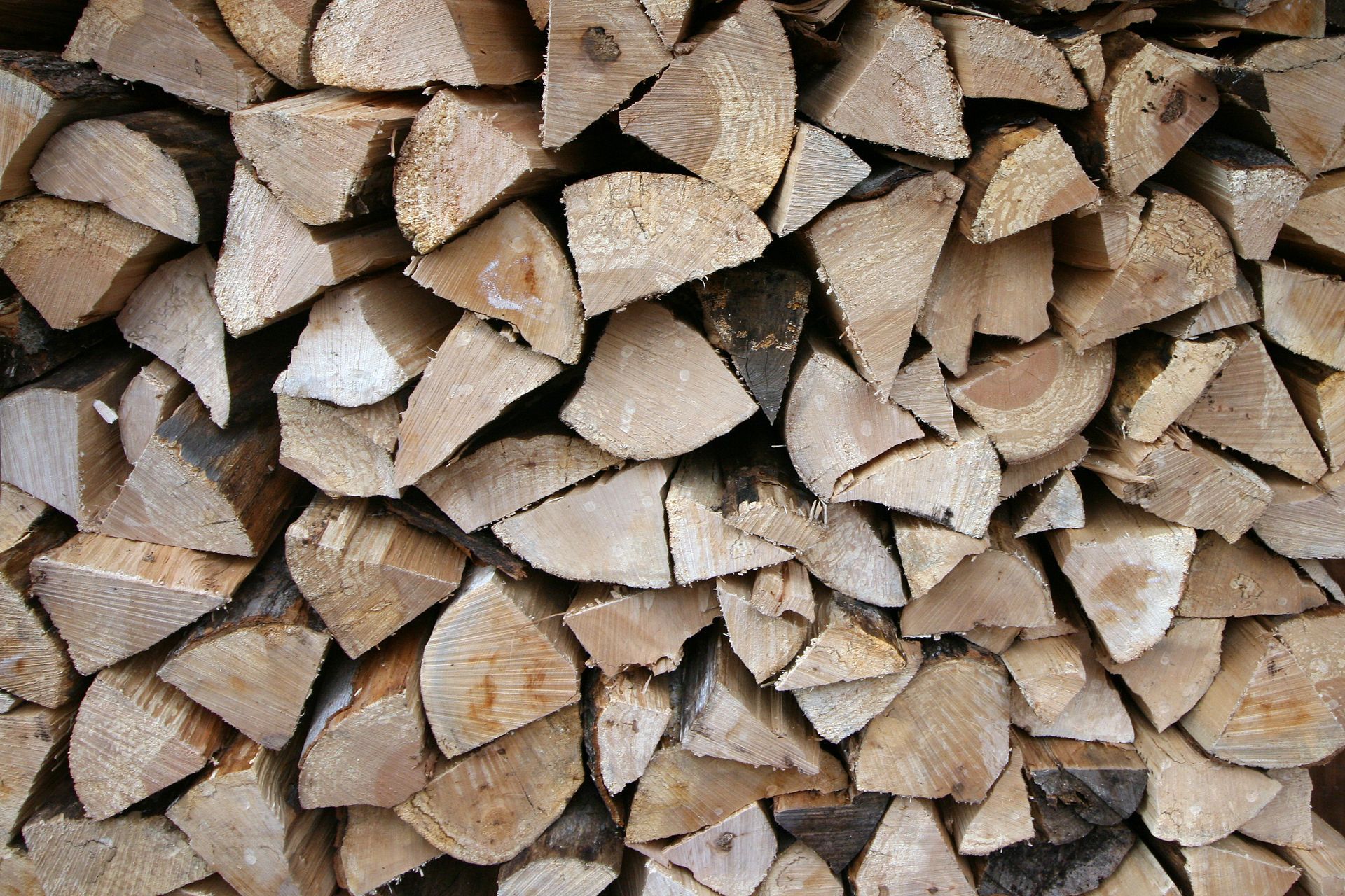 Pile of split firewood, stacked neatly, varying light browns.
