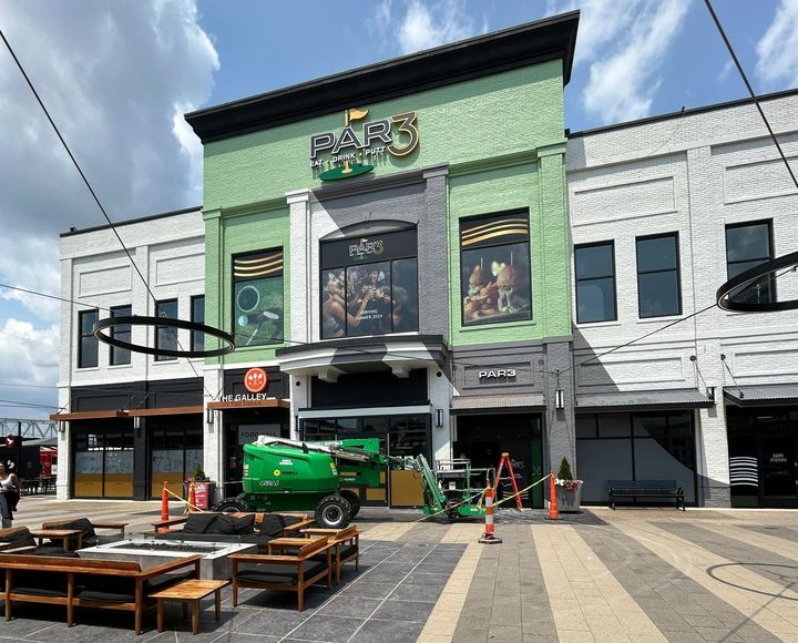 Two men are painting the side of a building. A green tractor is parked in front of a green and white building.