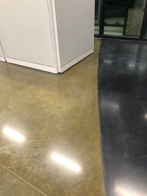 A close up of a shiny concrete floor with a cubicle in the background.