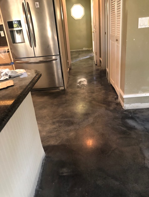 A kitchen with a stainless steel refrigerator and a black concrete floor.