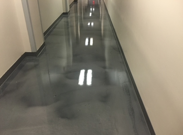 A long hallway with a shiny concrete floor and two lights on the walls.