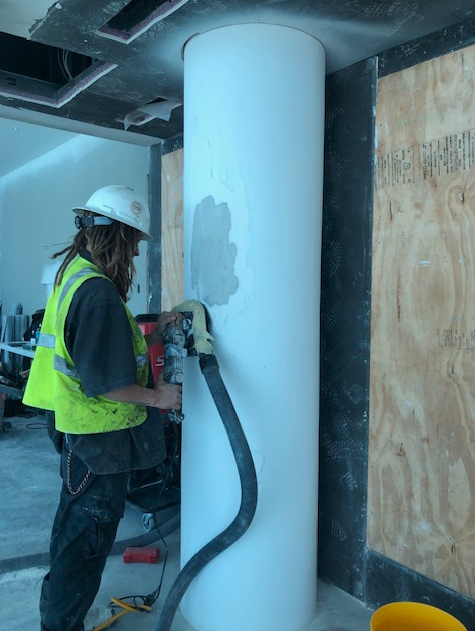 A man wearing a hard hat and safety vest is working on a pillar
