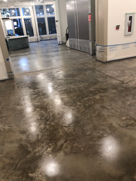 A shiny concrete floor in a room with a refrigerator in the background.