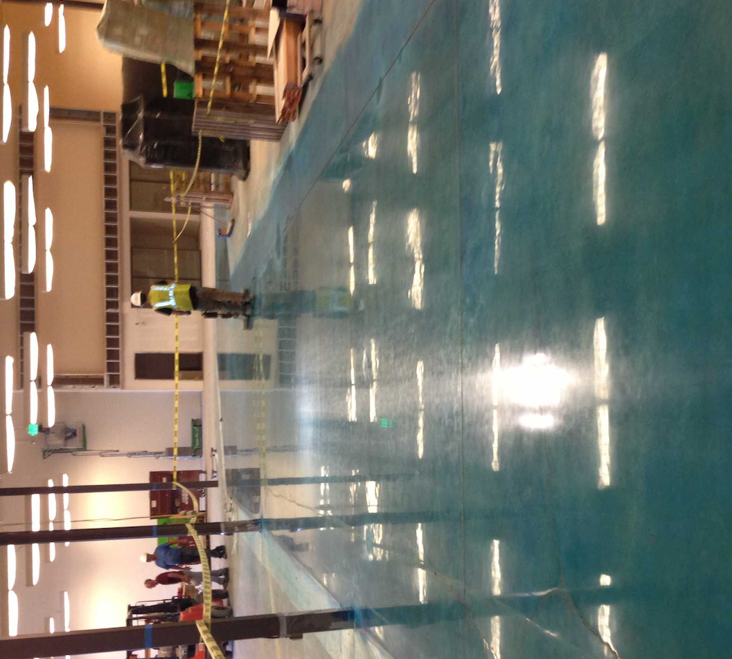 A man in a hard hat is standing in front of a large swimming pool
