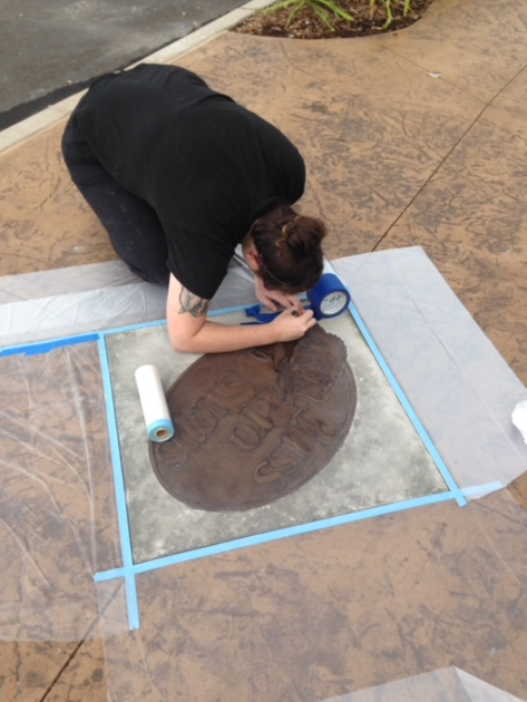 A woman is kneeling down on a concrete surface with a piece of tape on it