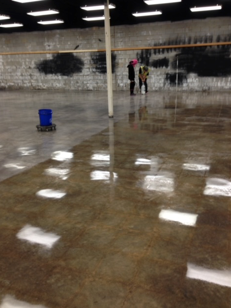 Two people are standing in a large empty room with a vacuum cleaner on the floor.