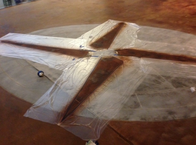 A wooden cross is wrapped in plastic on a concrete floor.