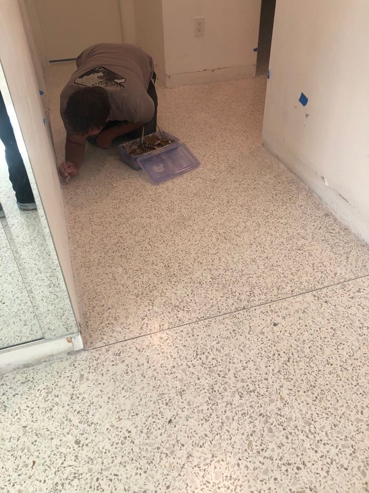 A man is kneeling on a white tiled floor in a hallway.