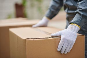 A person wearing white gloves is holding a cardboard box.