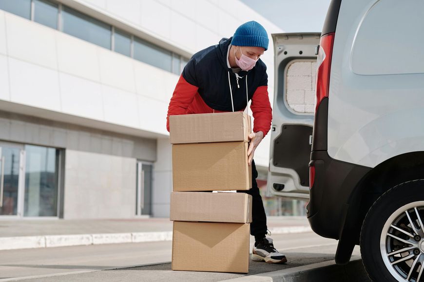 A delivery man wearing a mask is loading boxes into a van.