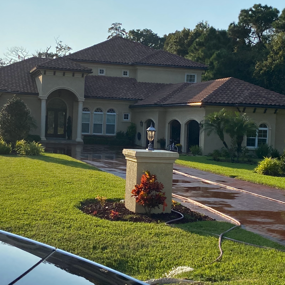 Large beige house with red tile roof, green lawn, and a pillar with a lamp in the foreground.
