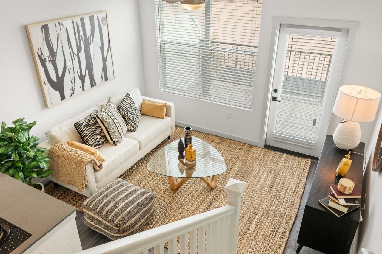 Living room in an apartment with a white sofa, glass coffee table, and woven rug.