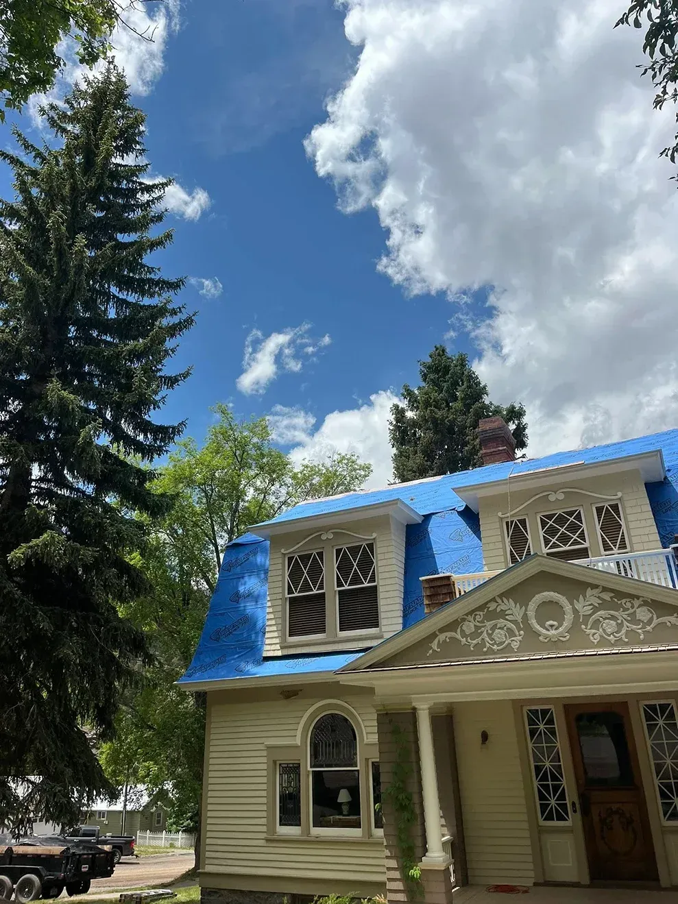 Victorian house with blue roof under a partly cloudy sky. Tall tree on the left.