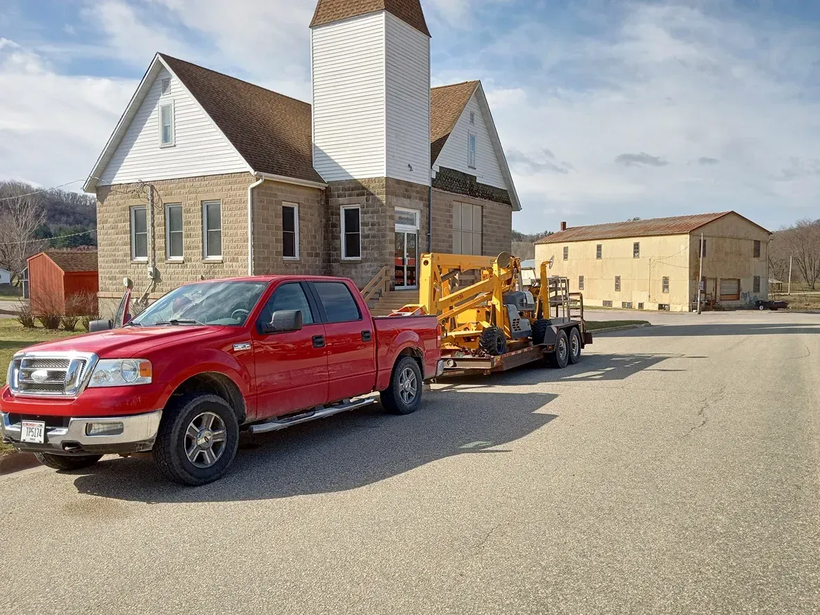 Red truck towing construction equipment in front of a stone building with a steeple.
