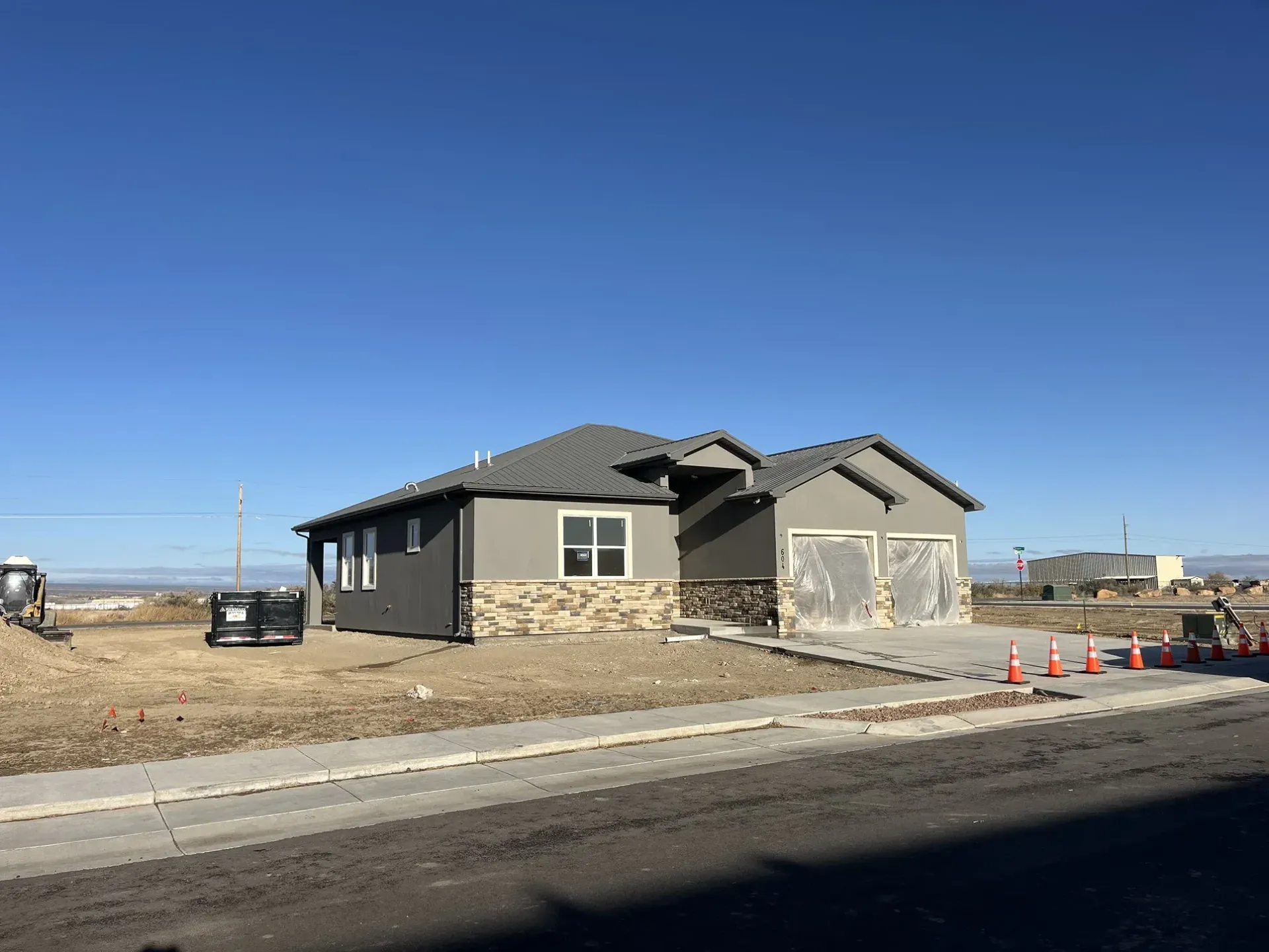New home under construction with gray siding, stone accents, and a two-car garage, set against a blue sky.