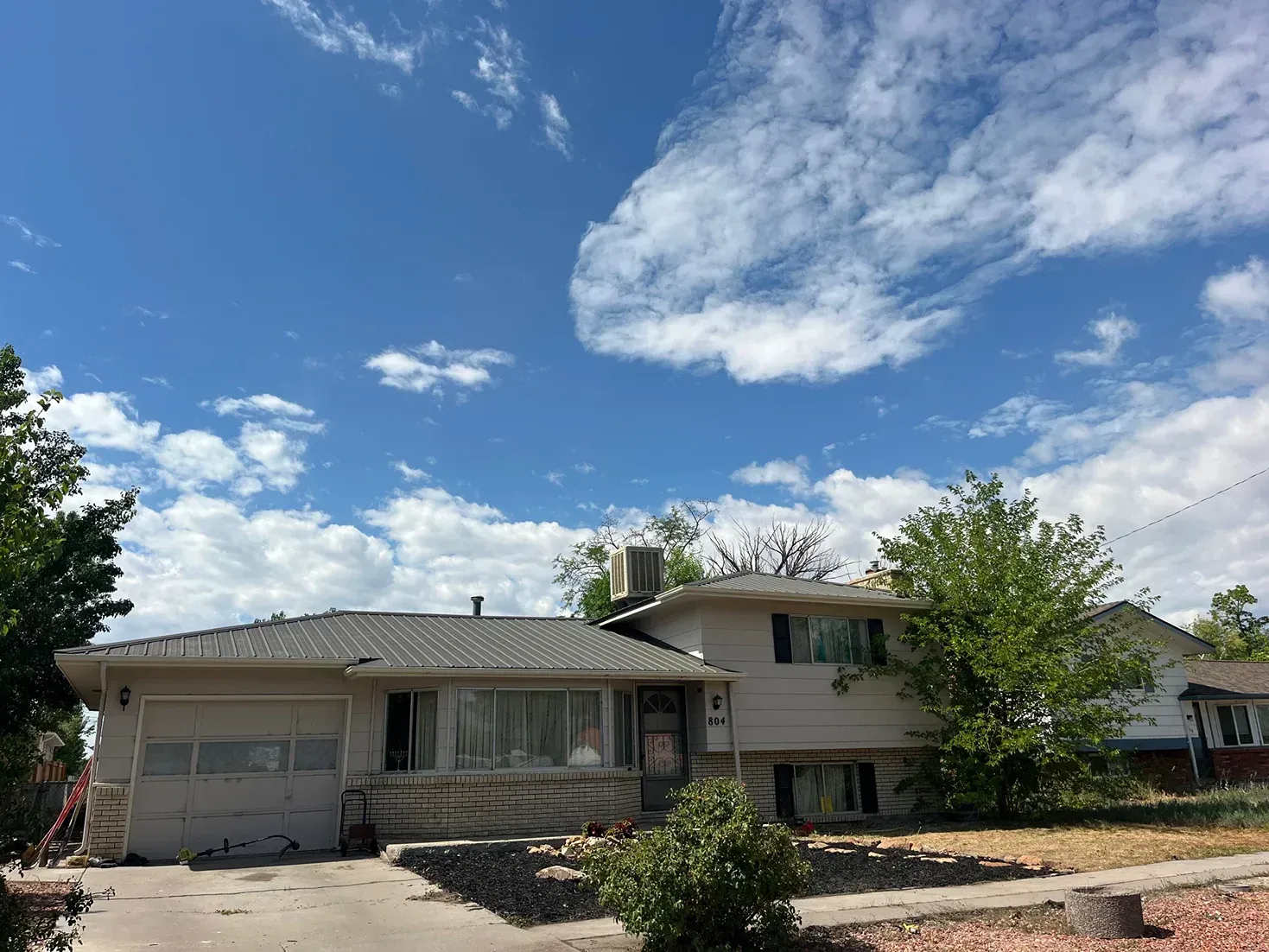 House with a garage and tree under a cloudy blue sky.
