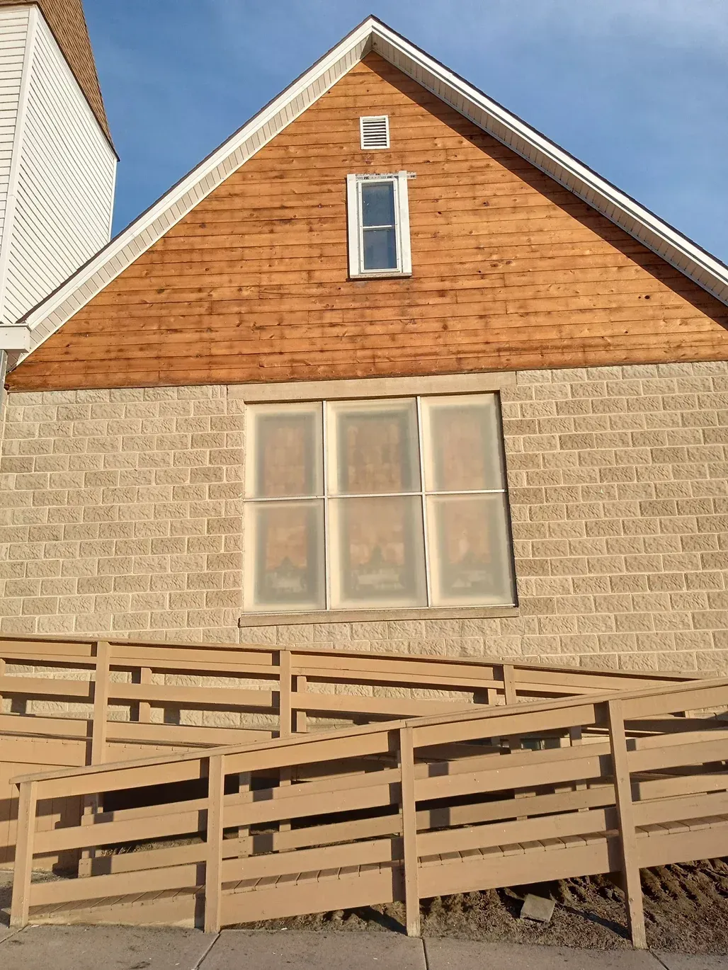 Tan building with a wooden ramp; brick-like exterior and a gable roof with small window and vent.