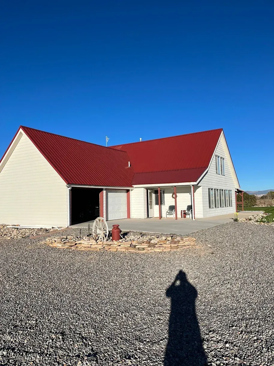 House with a red roof, white siding, and garage under a clear, blue sky. A shadow is in the foreground.