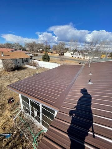 Brown metal roof on a house, sunny day, blue sky with clouds.