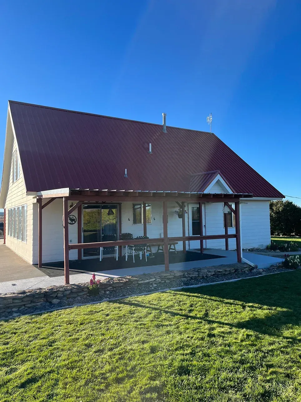 White house with a red roof, a wooden porch, and a blue sky.