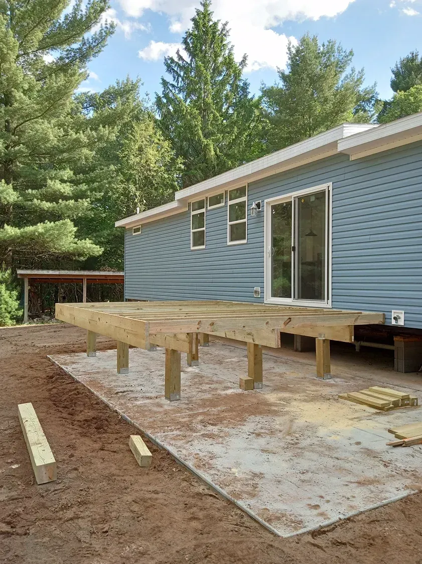 Wooden deck frame under construction outside a blue-sided house with a sliding glass door.