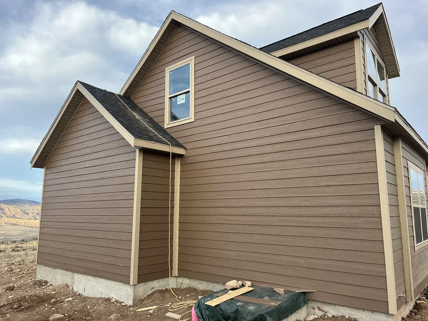 Brown house with beige trim and dark roof under a cloudy sky.