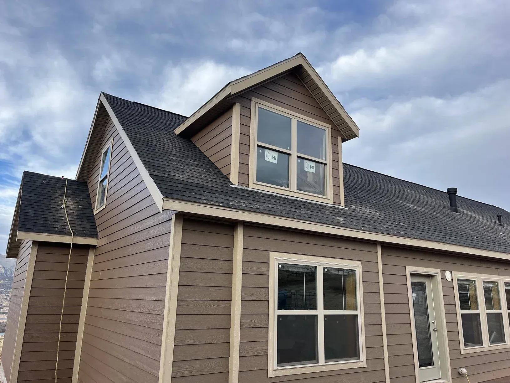 Brown house with dark roof and dormer, under cloudy sky.