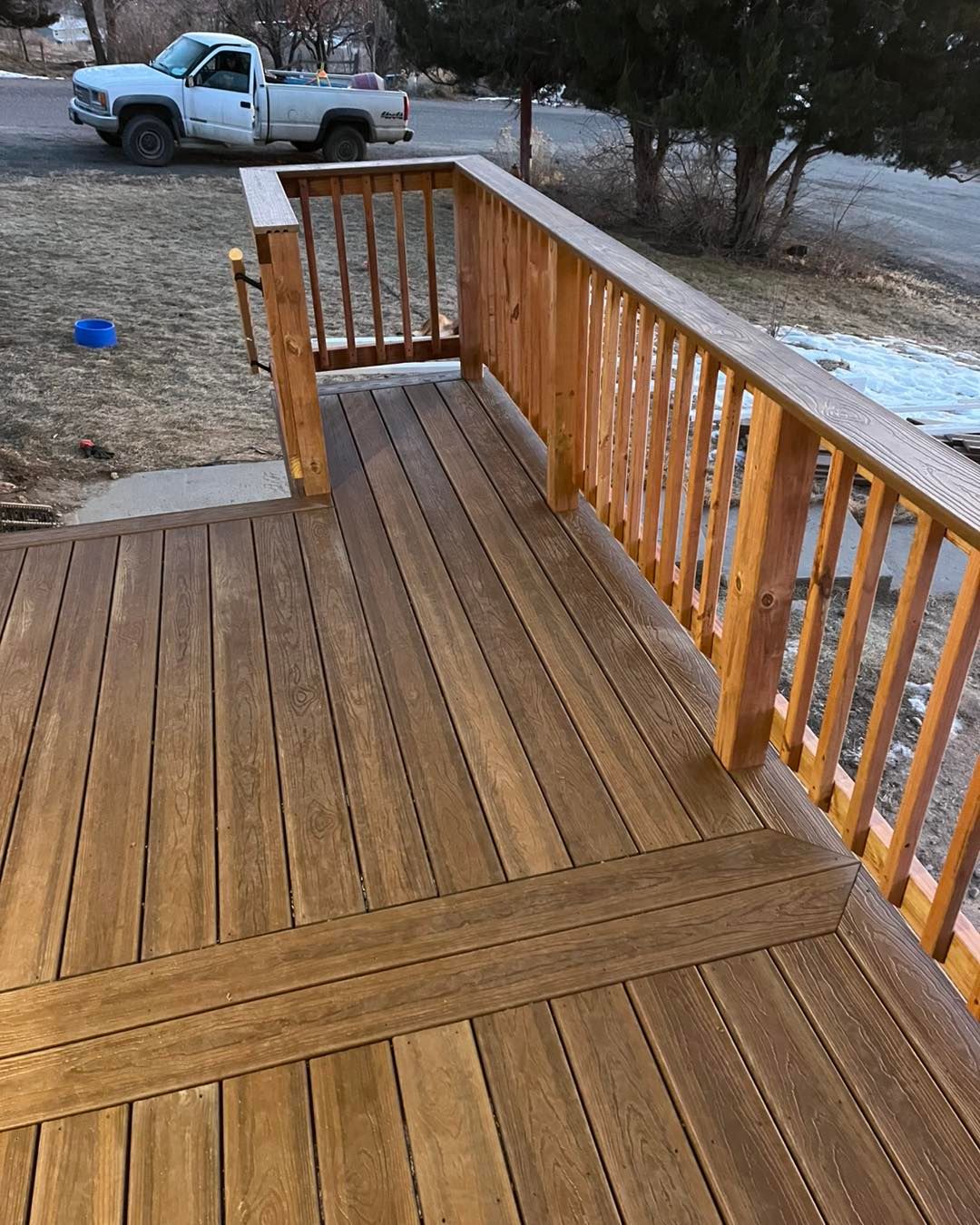 Wooden deck with railing. A truck is parked nearby, a snowy, residential setting.