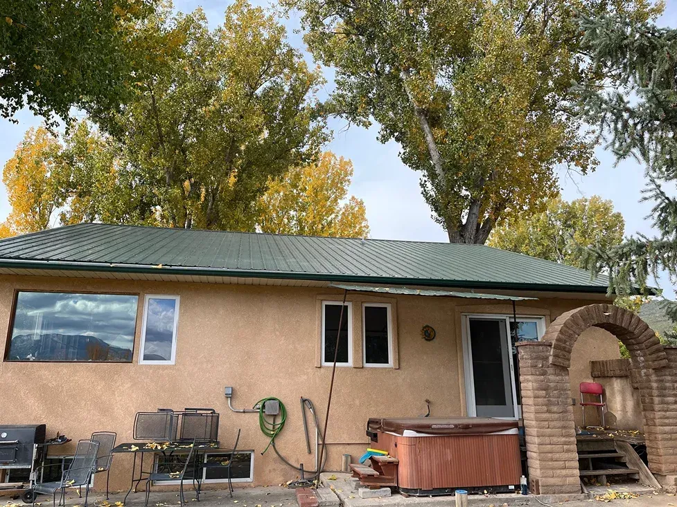 Tan house with green roof; trees with yellow leaves behind.  A hot tub and chairs sit outside.
