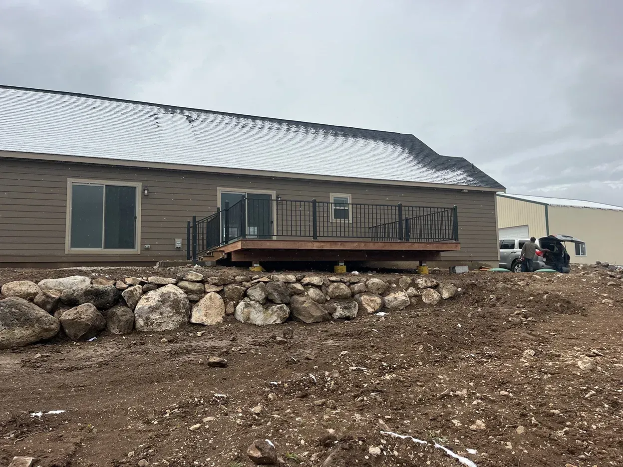 House with a deck, rock wall, and overcast sky.  Some snow on roof.