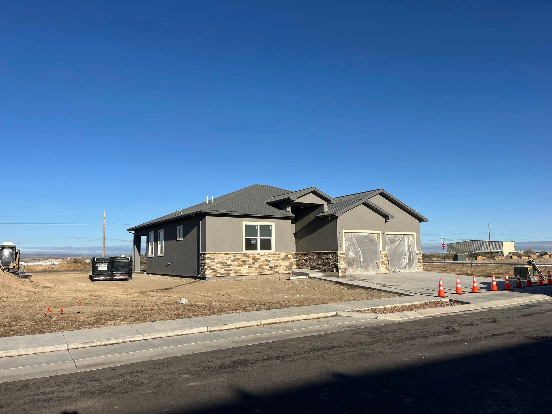 New house under construction with gray siding, stone accents, and a clear blue sky.