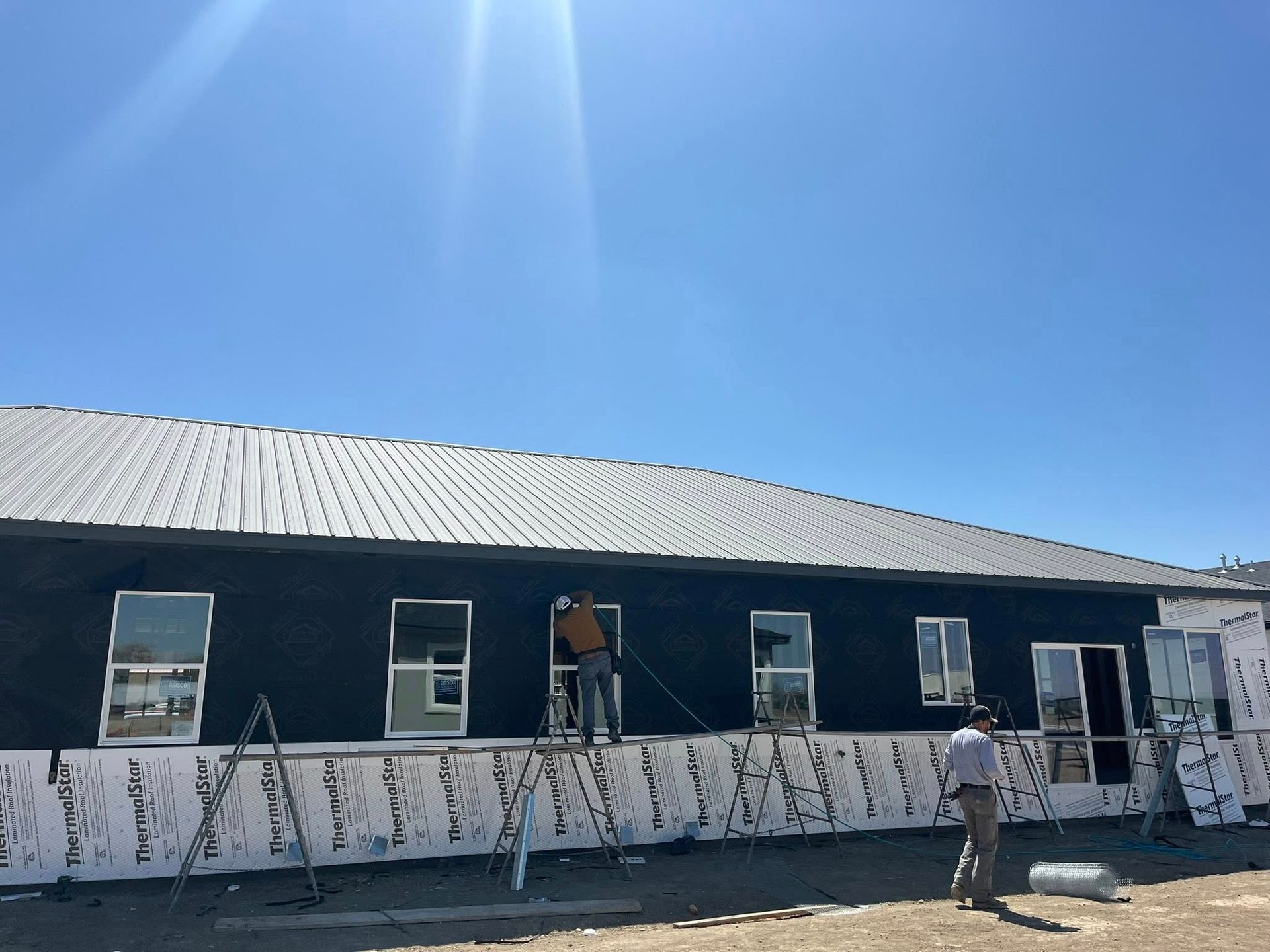 Construction workers on a building with a metal roof, installing windows on a sunny day.