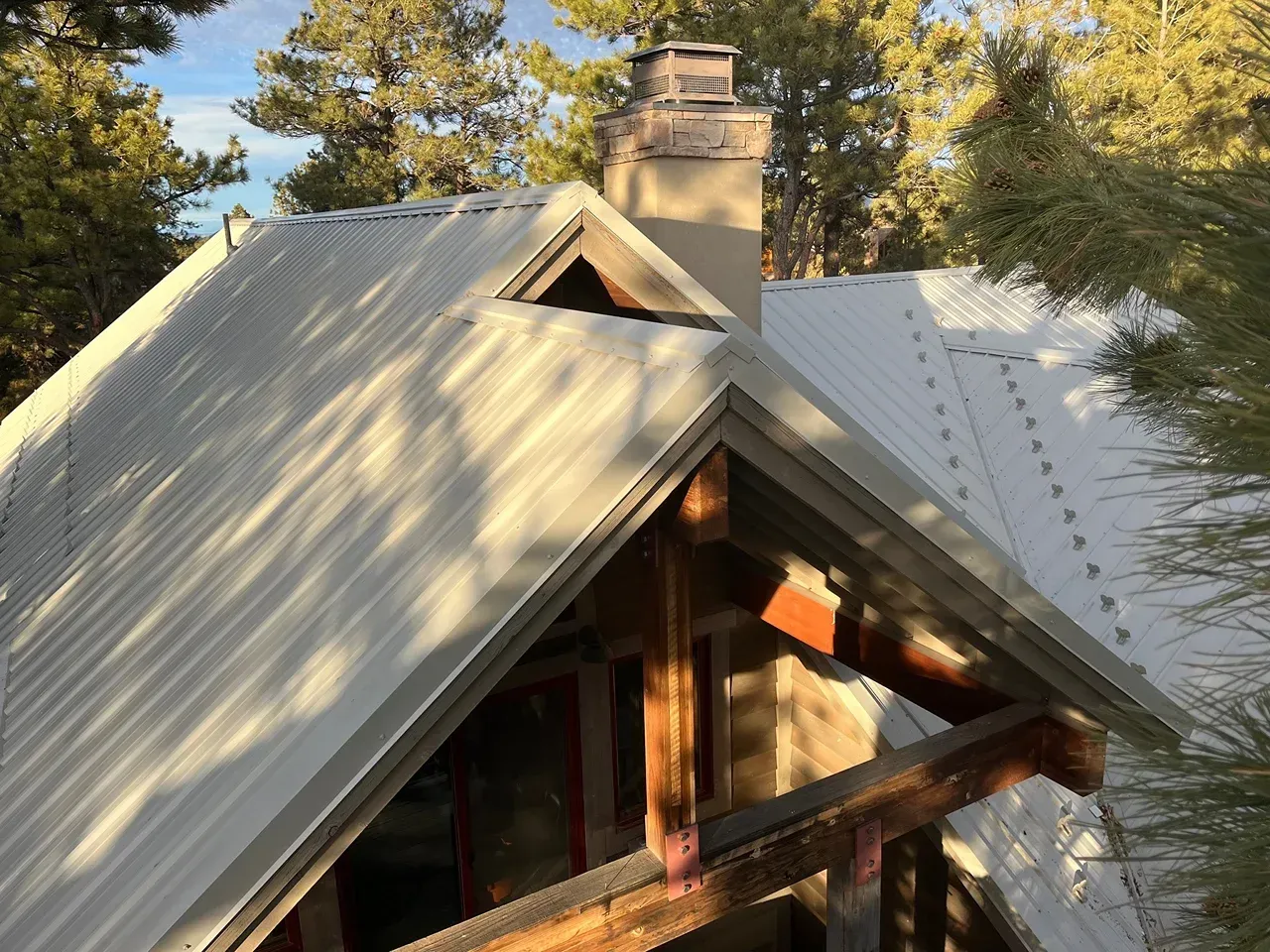 Metal roof of a cabin with a chimney, framed by trees.