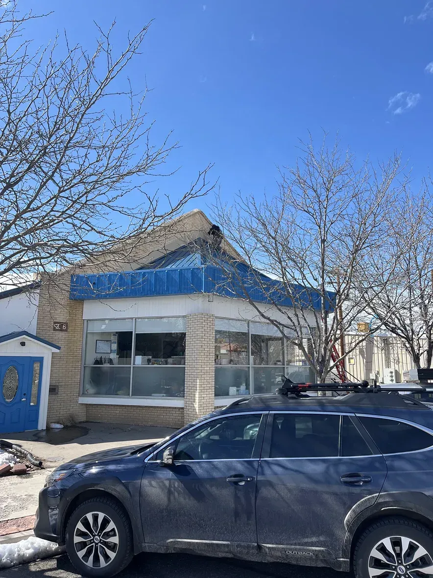 Blue-roofed commercial building with large windows and a car parked in front on a sunny day.