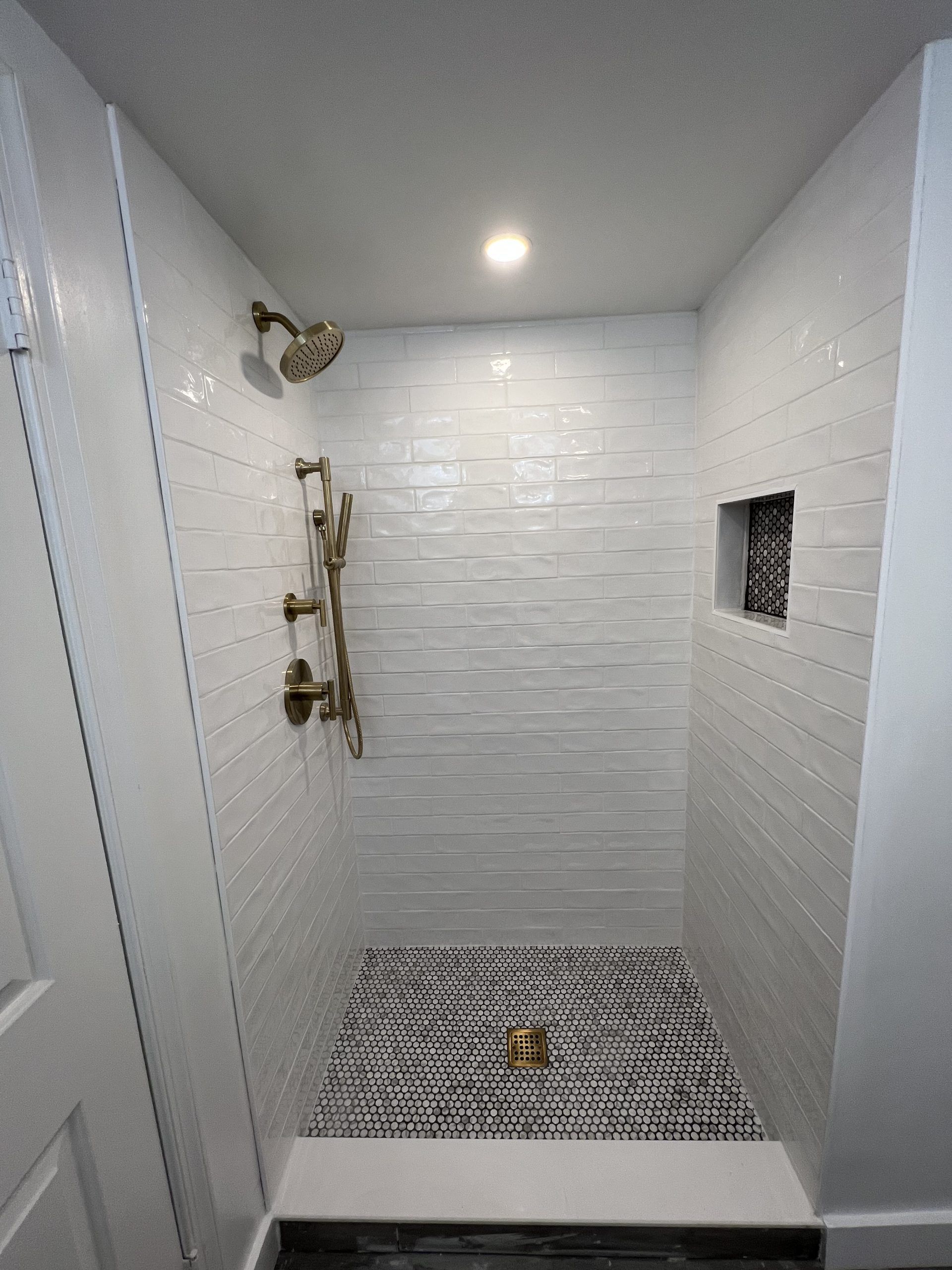 White tiled shower with bronze fixtures and black and white patterned floor.