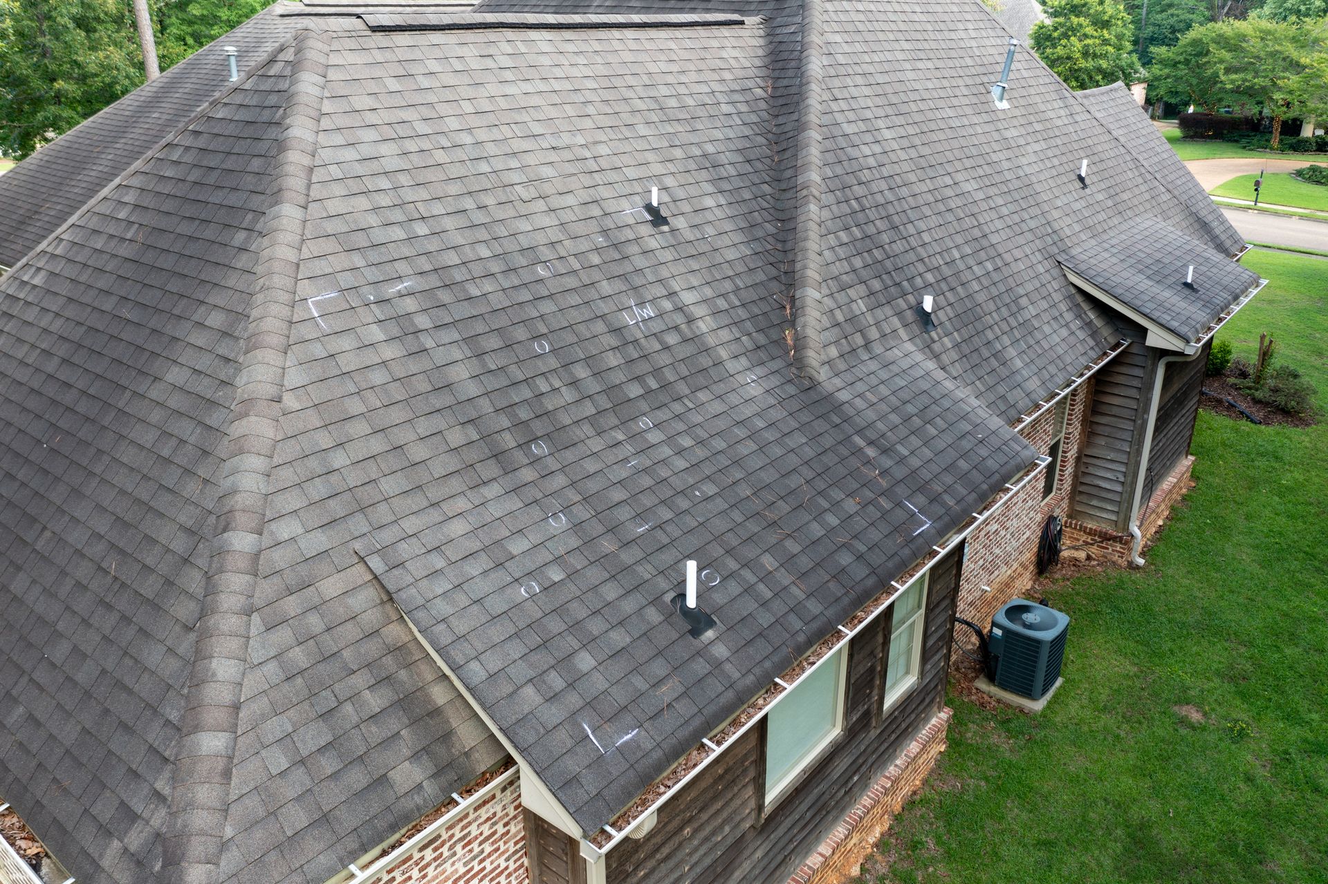 An aerial view of a house with a black roof and a blue air conditioner.