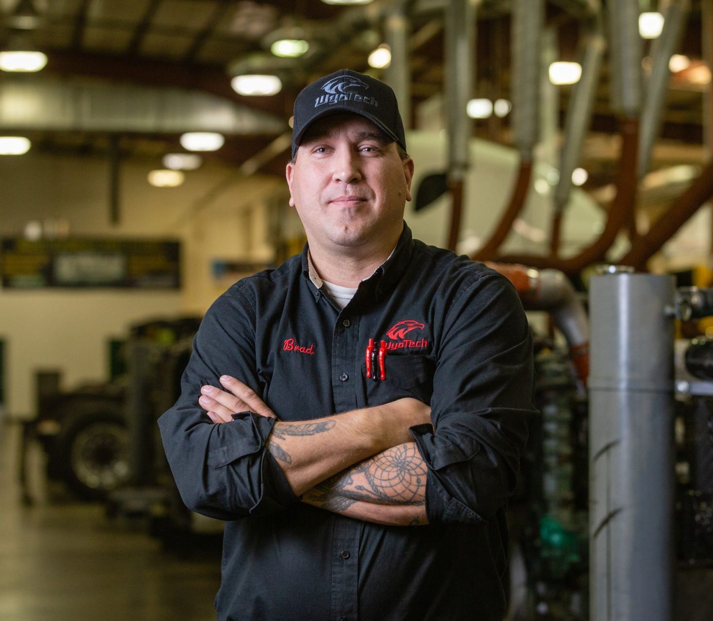 Brad Williams in a black shirt and hat is standing in a garage with his arms crossed.