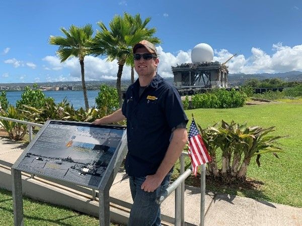 Jared standing in front of a sign with an American flag in Hawaii.