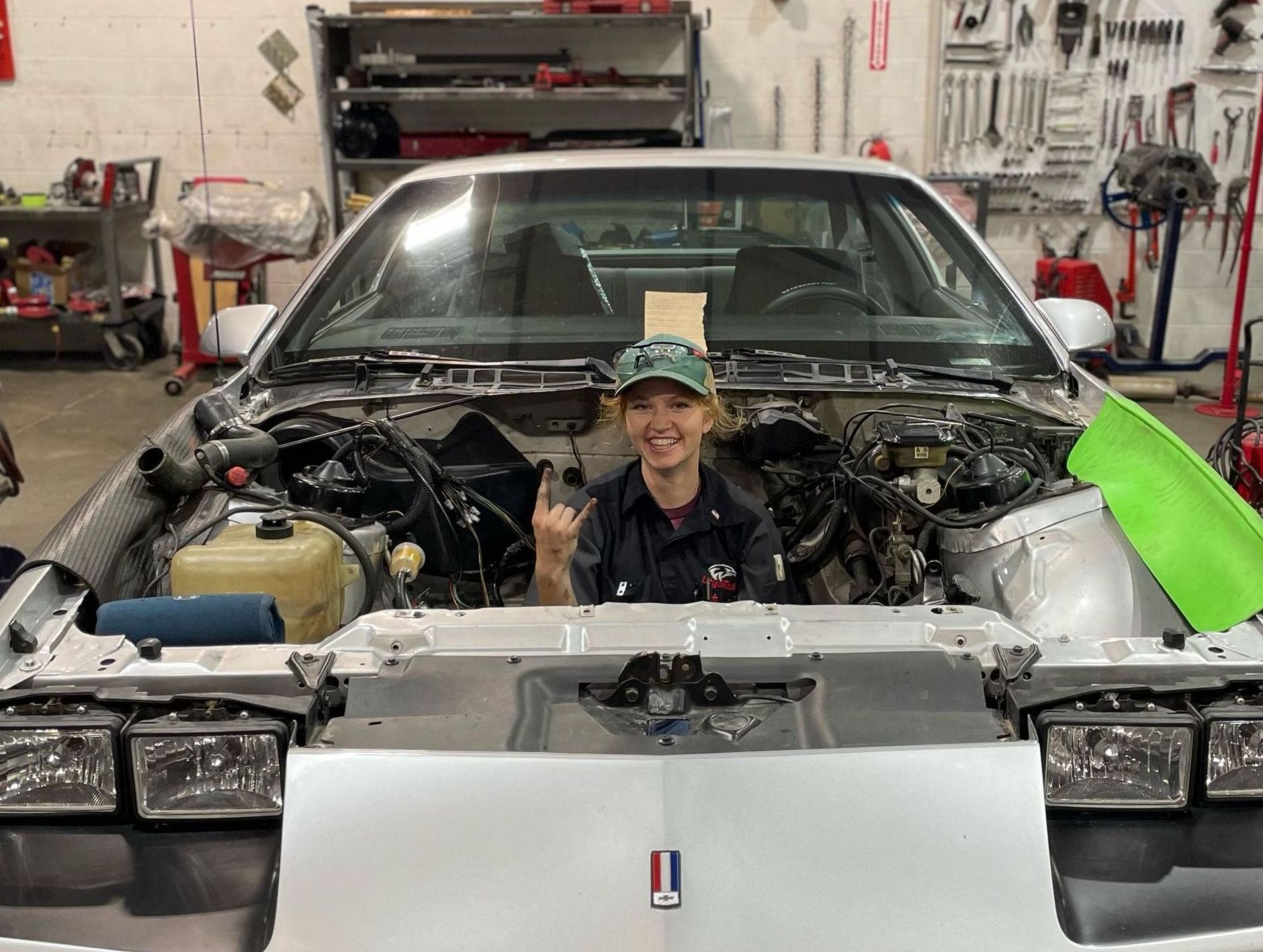 A woman is sitting in the engine of a car in a garage.