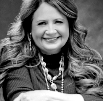 A black and white photo of a woman smiling with her hand on her face.