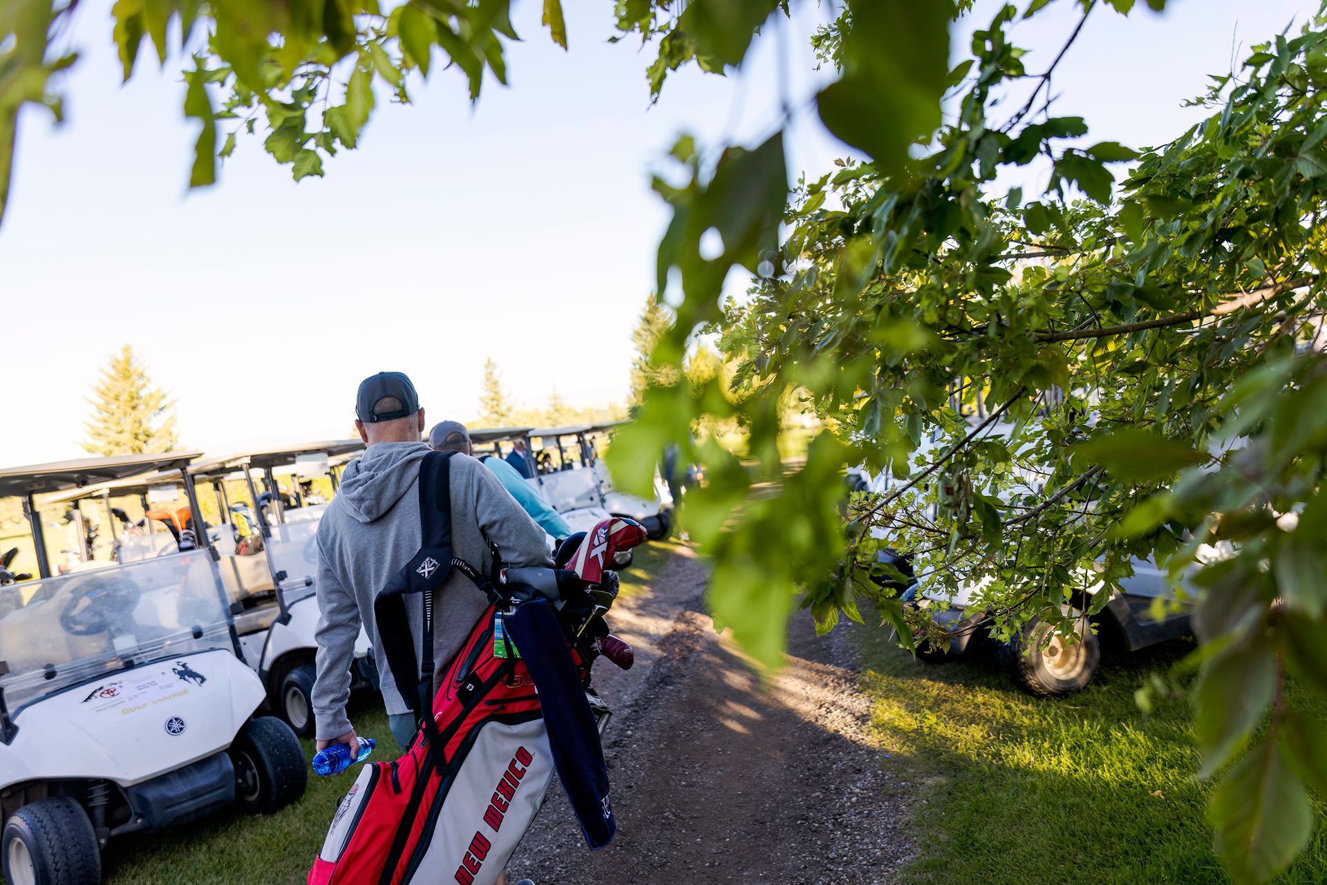 A man is walking down a dirt road carrying a golf bag.