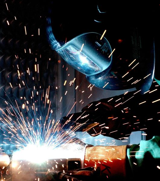A man is welding a piece of metal in a dark room