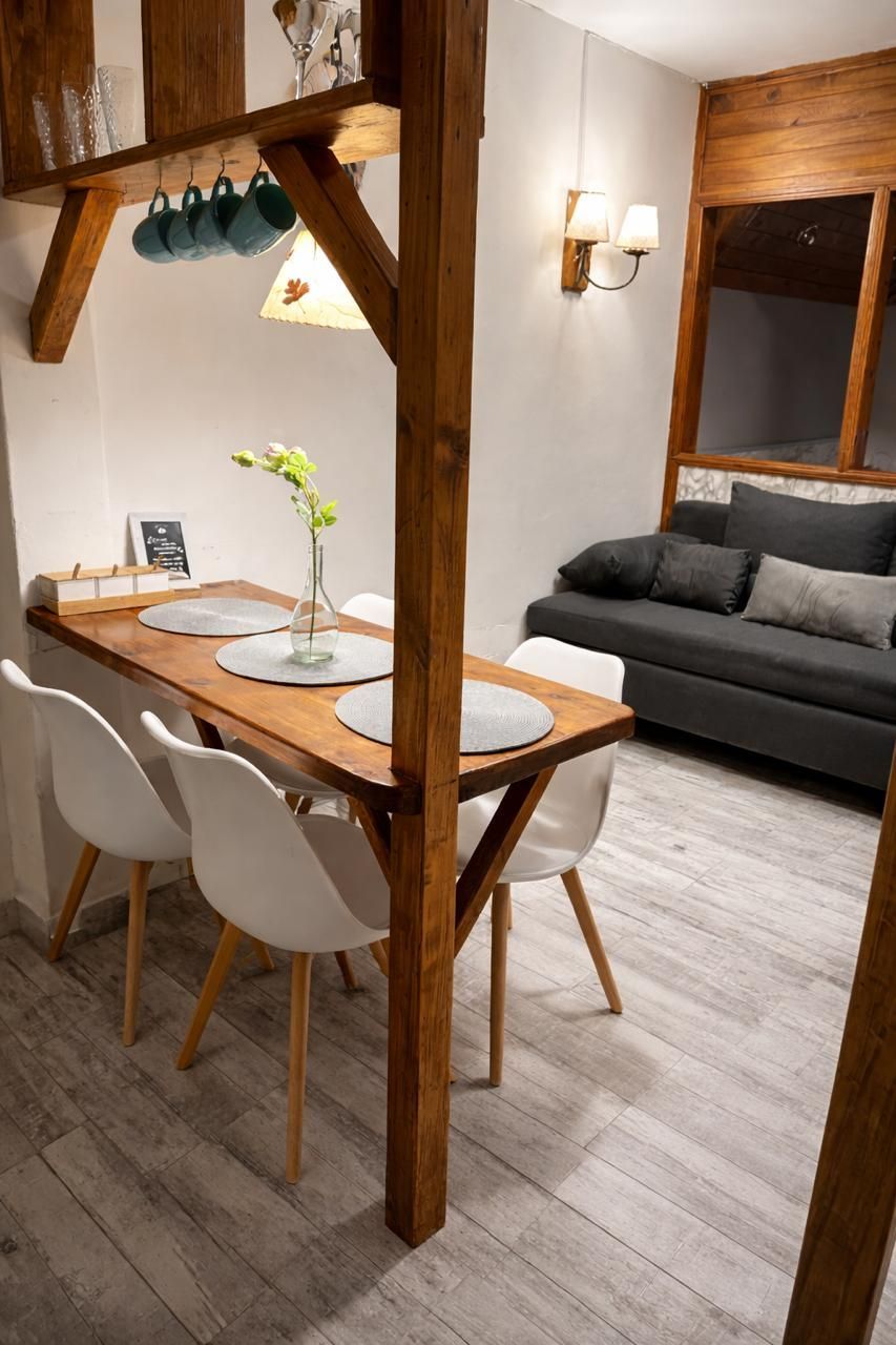 Acogedor salón-comedor con mesa de madera, sillas blancas, sofá gris y cálidos detalles en madera.