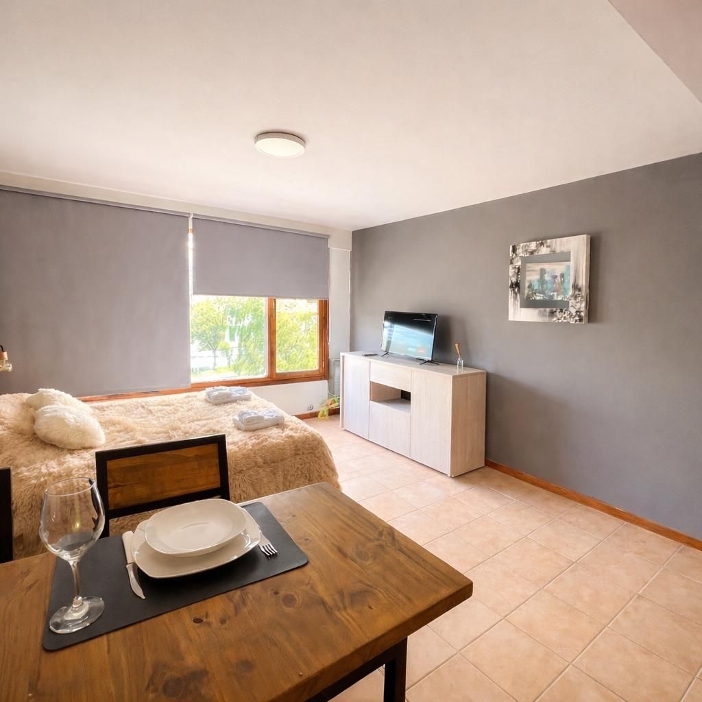 Dormitorio moderno con paredes grises, una cama, mesa auxiliar de madera, mueble para la televisión y luz de ventana.