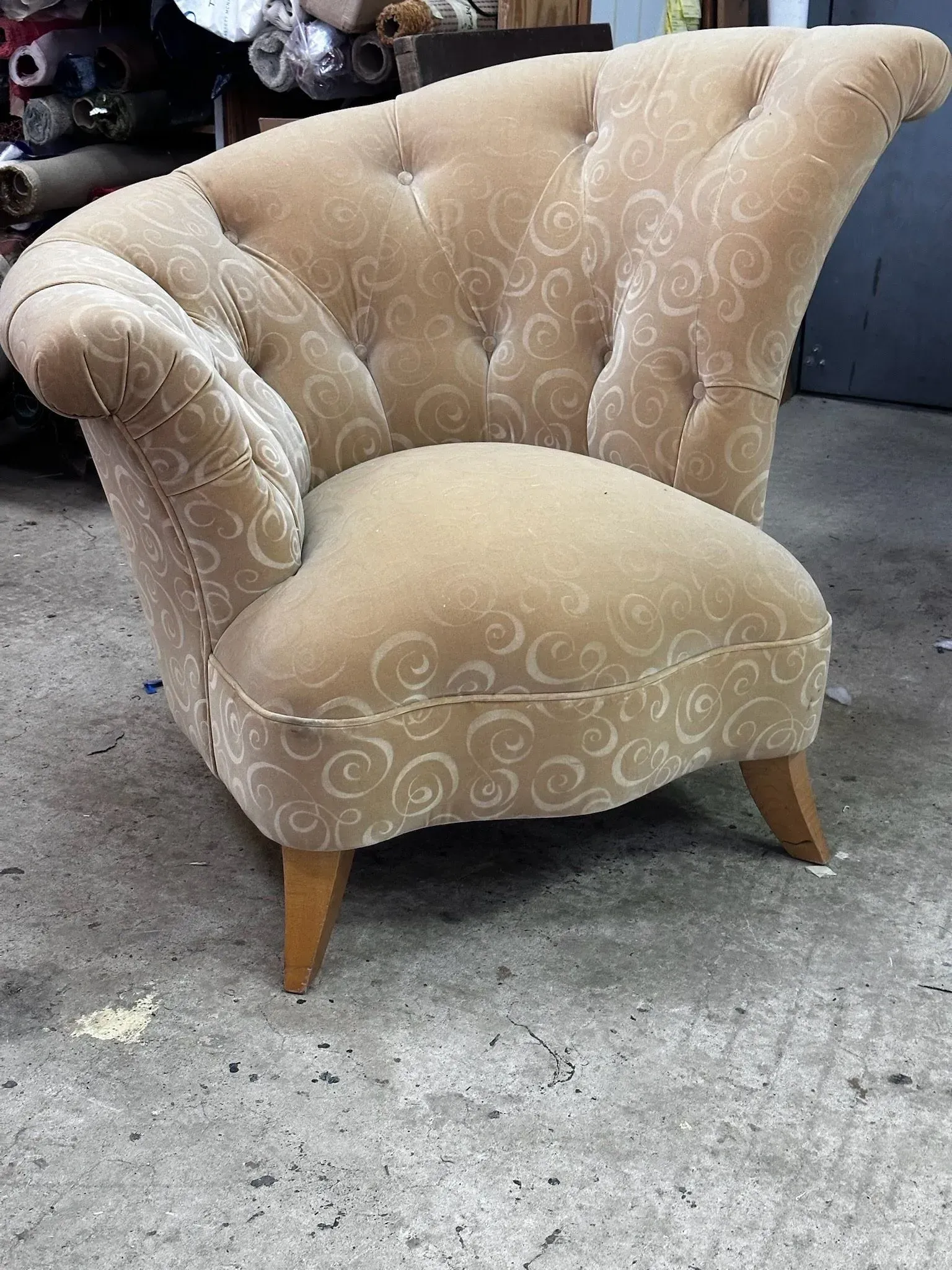 Beige accent chair with tufted back and swirl-patterned fabric sitting in a workshop.