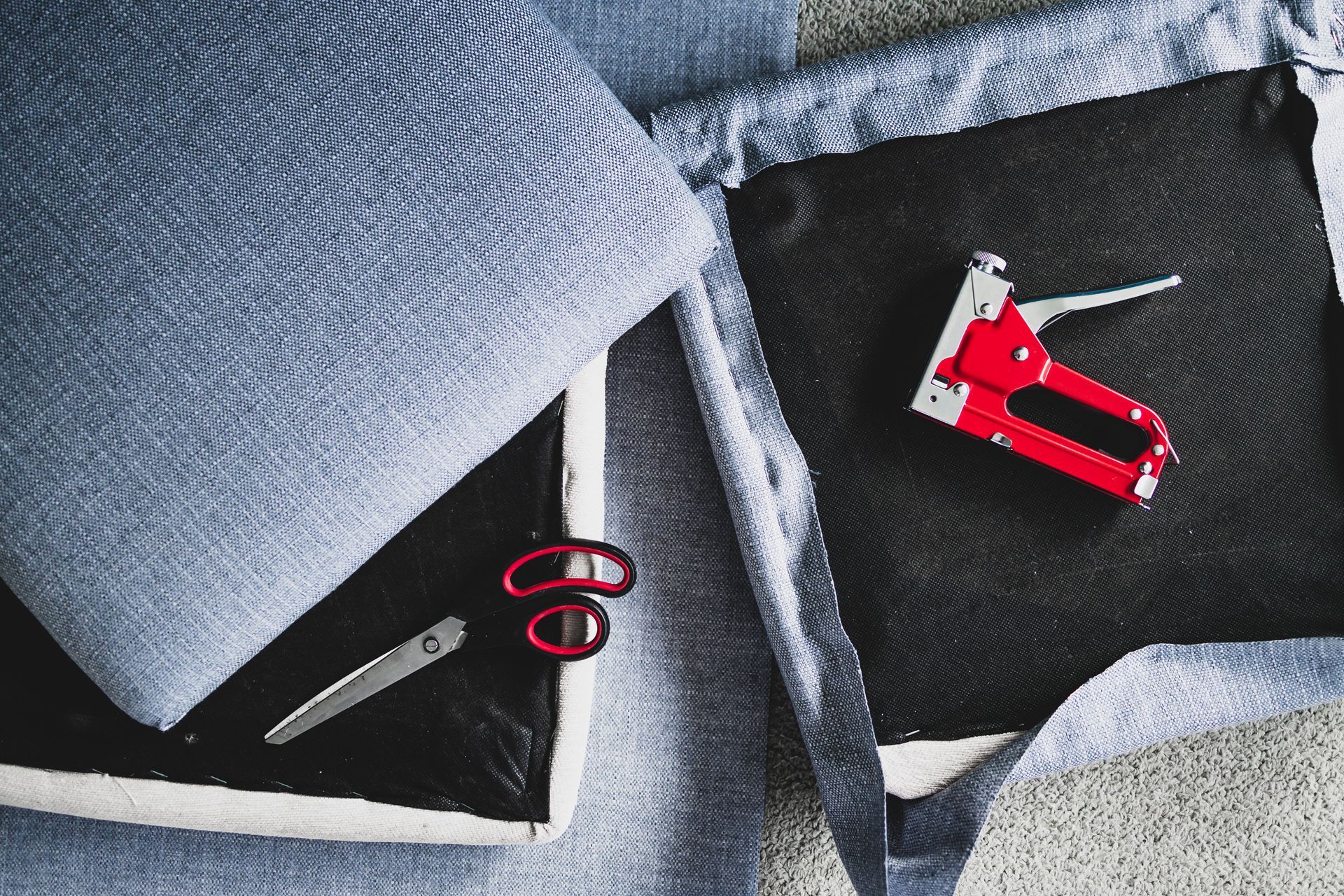 Upholstery project with fabric, scissors, and a staple gun arranged around seat cushions.