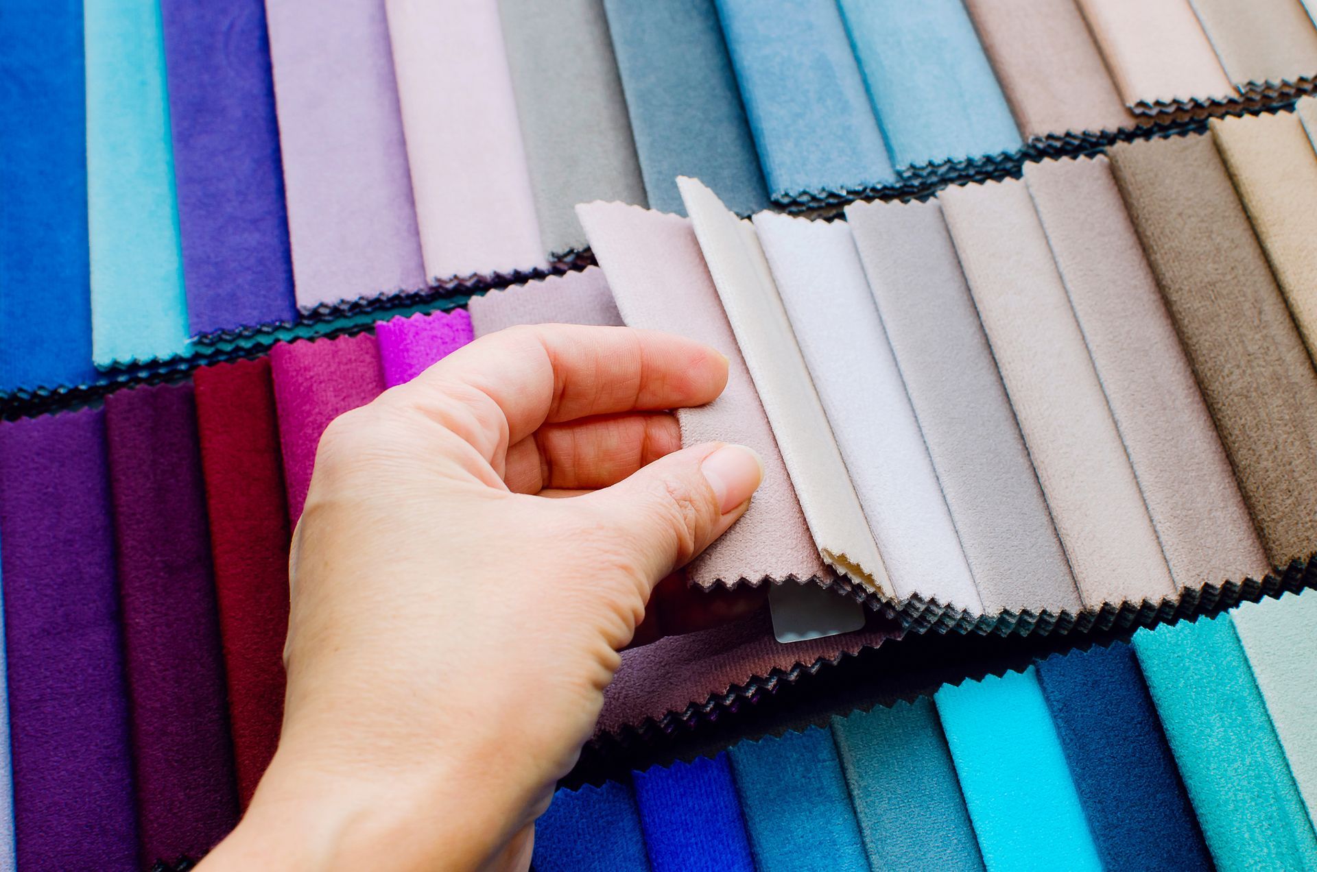 Hand selecting a fabric sample from a display of colorful upholstery swatches.