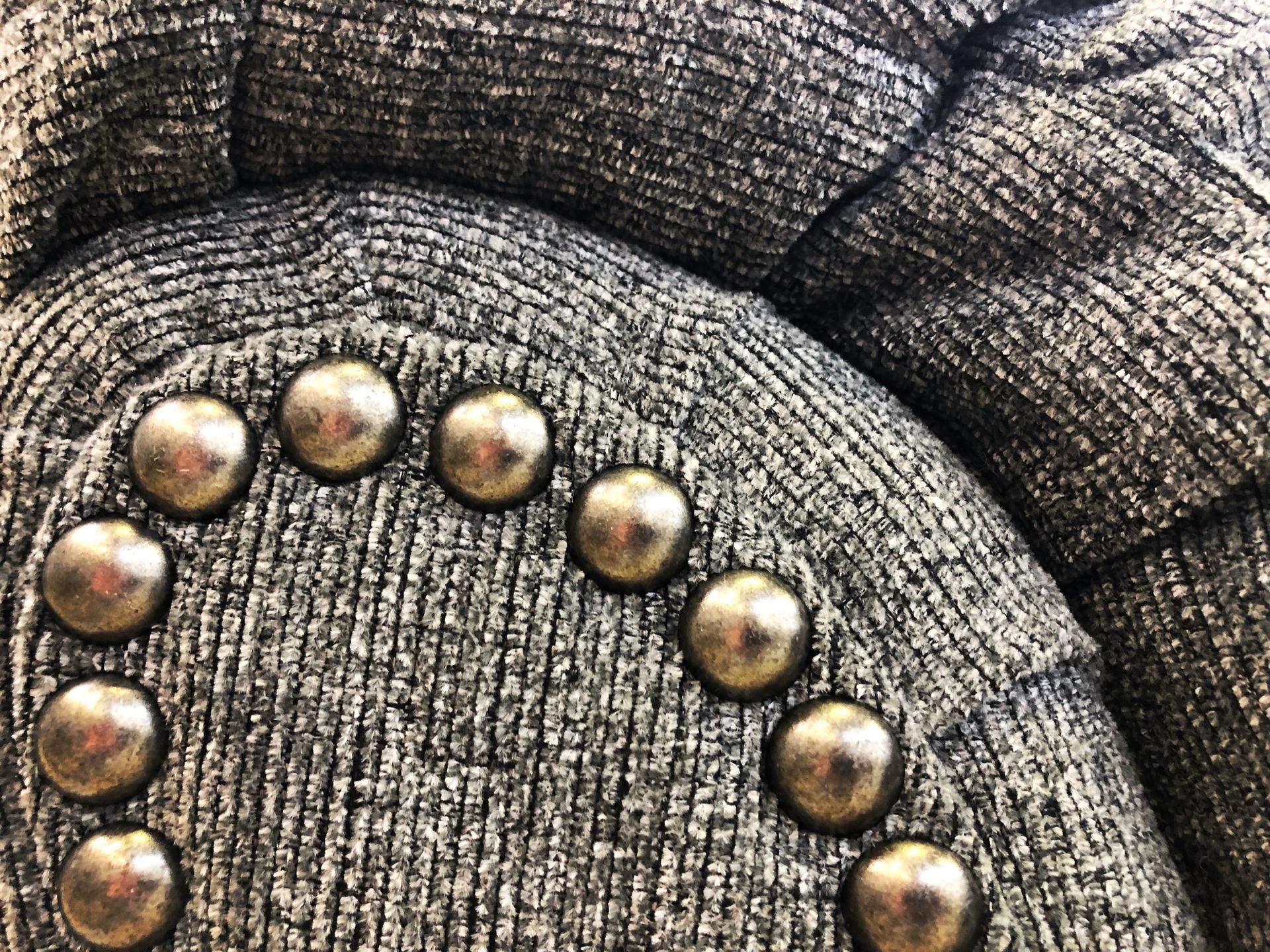 Closeup of the armrest of a grey upholstered chair with decorative metal rivets.