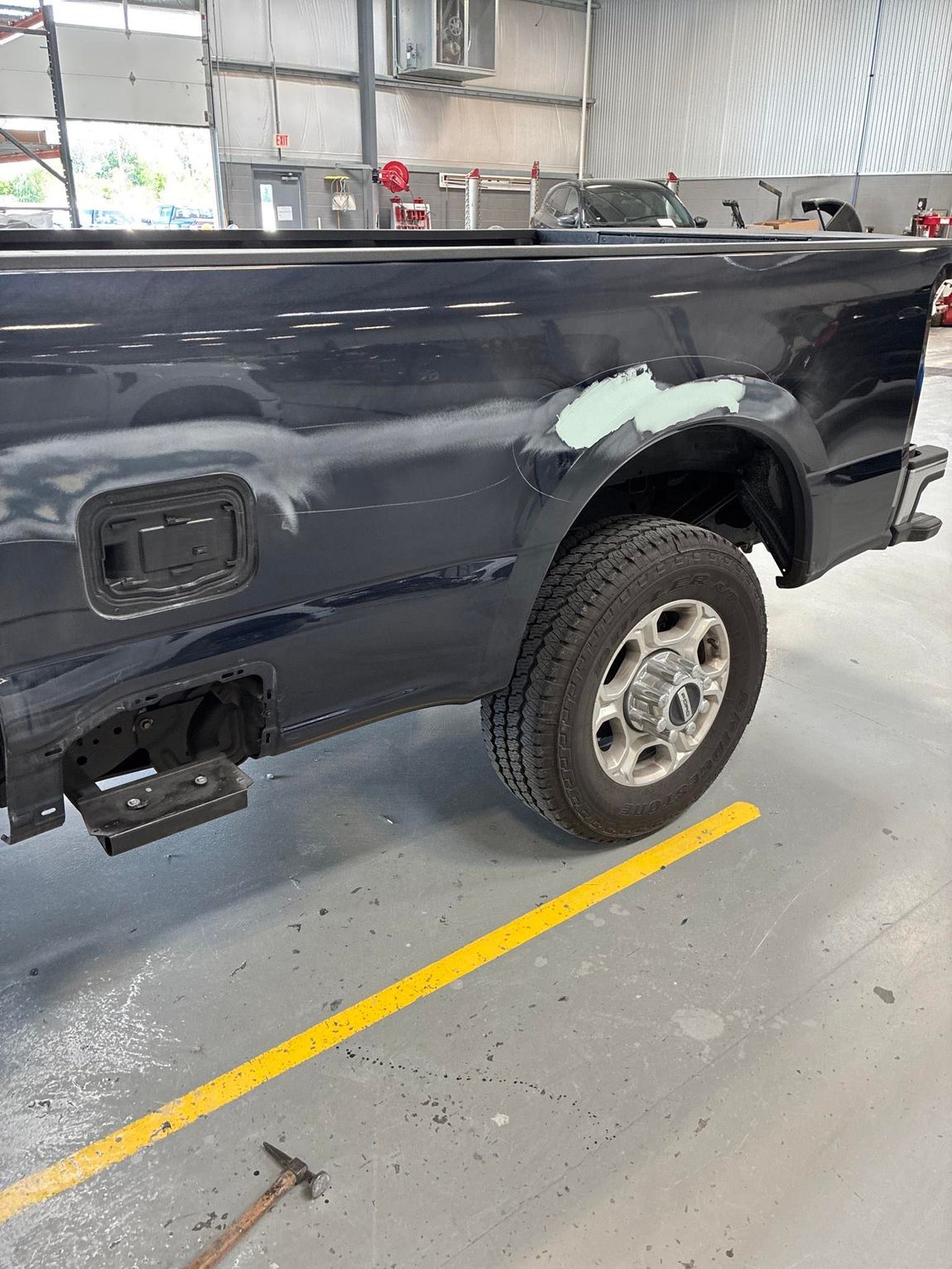Dark blue truck bed, partially repaired, in a workshop. Wheel and step visible.