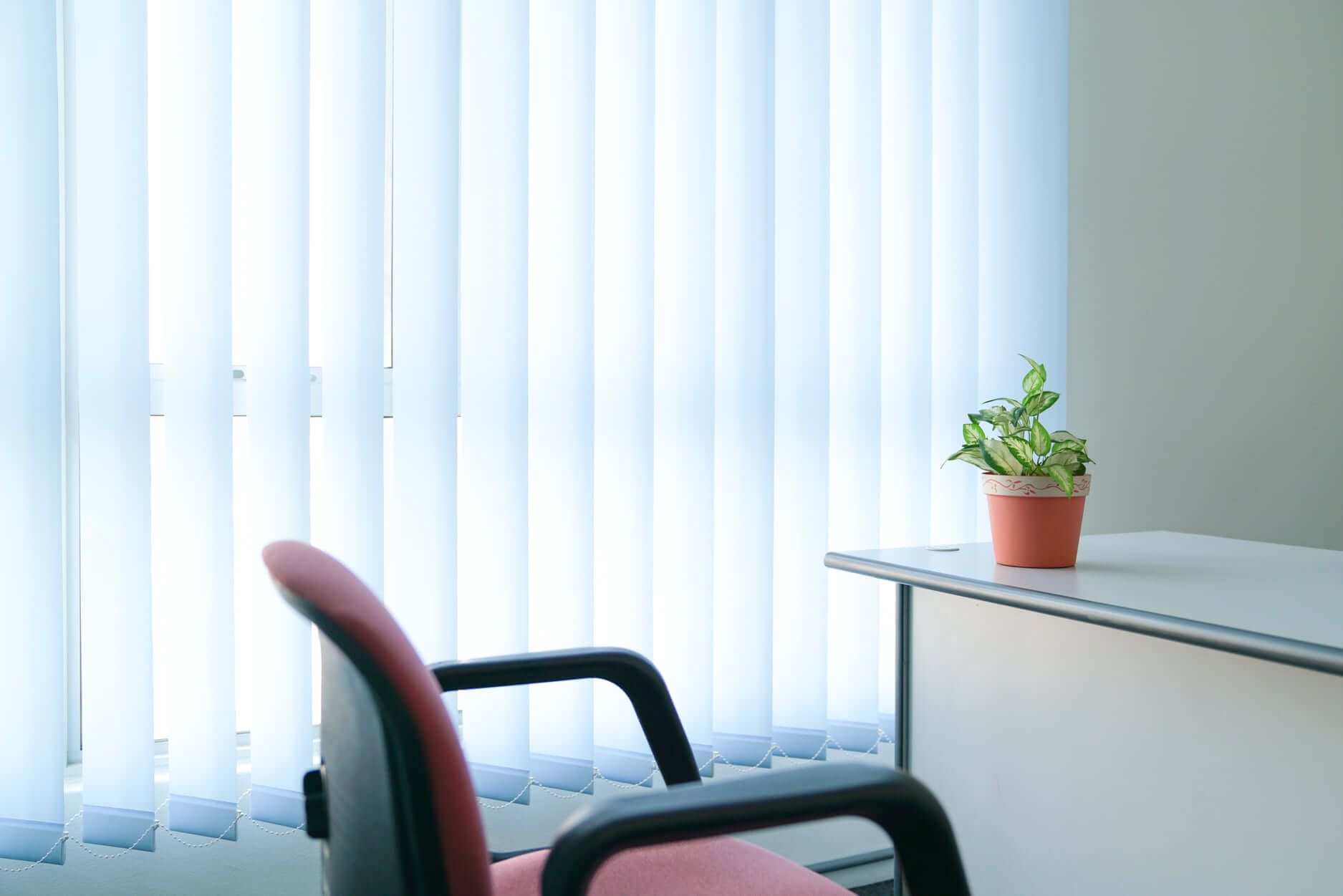 A wooden chair and desk placed in front of a window with blinds.